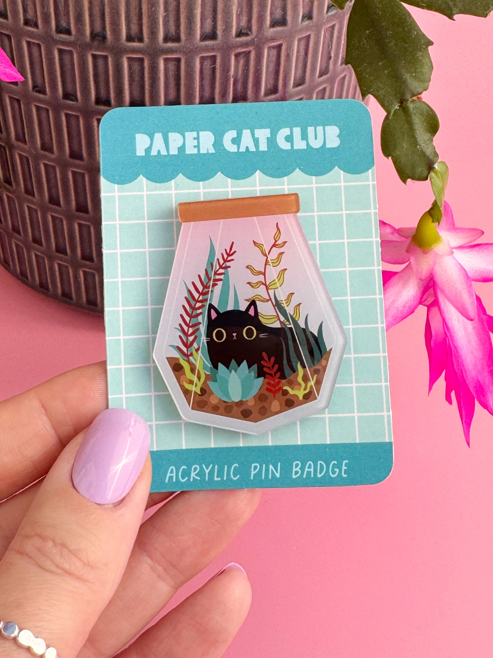 A super cute and kawaii acrylic pin badge on a cute backing card featuring a black cat in a terrarium.