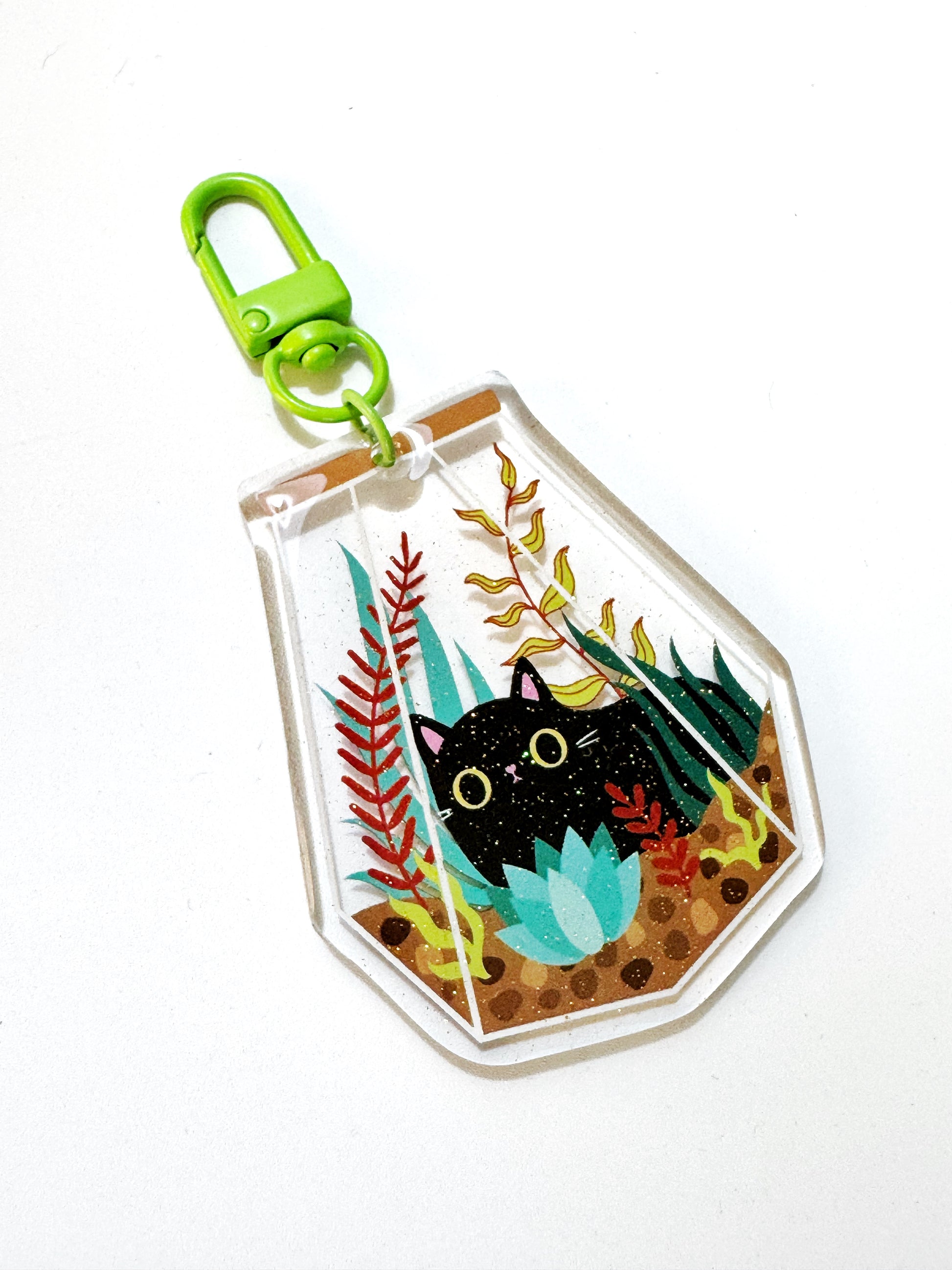 Cute Cat in a Terrarium Keyring – a kawaii acrylic keychain featuring an adorable chubby cat inside a glass terrarium with glitter accents. Perfect for cat lovers, kawaii style fans, and cottagecore aesthetics. A chunky, eye-catching keyring with durable green hardware, ideal as a cat lover gift or cute accessory