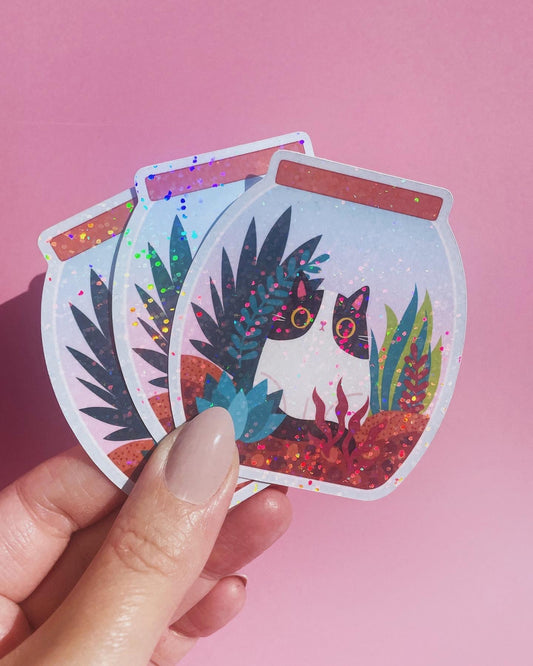 Sparkly vinyl cat sticker with a cat in a terrarium, perfect for laptops, journals, and water bottles.