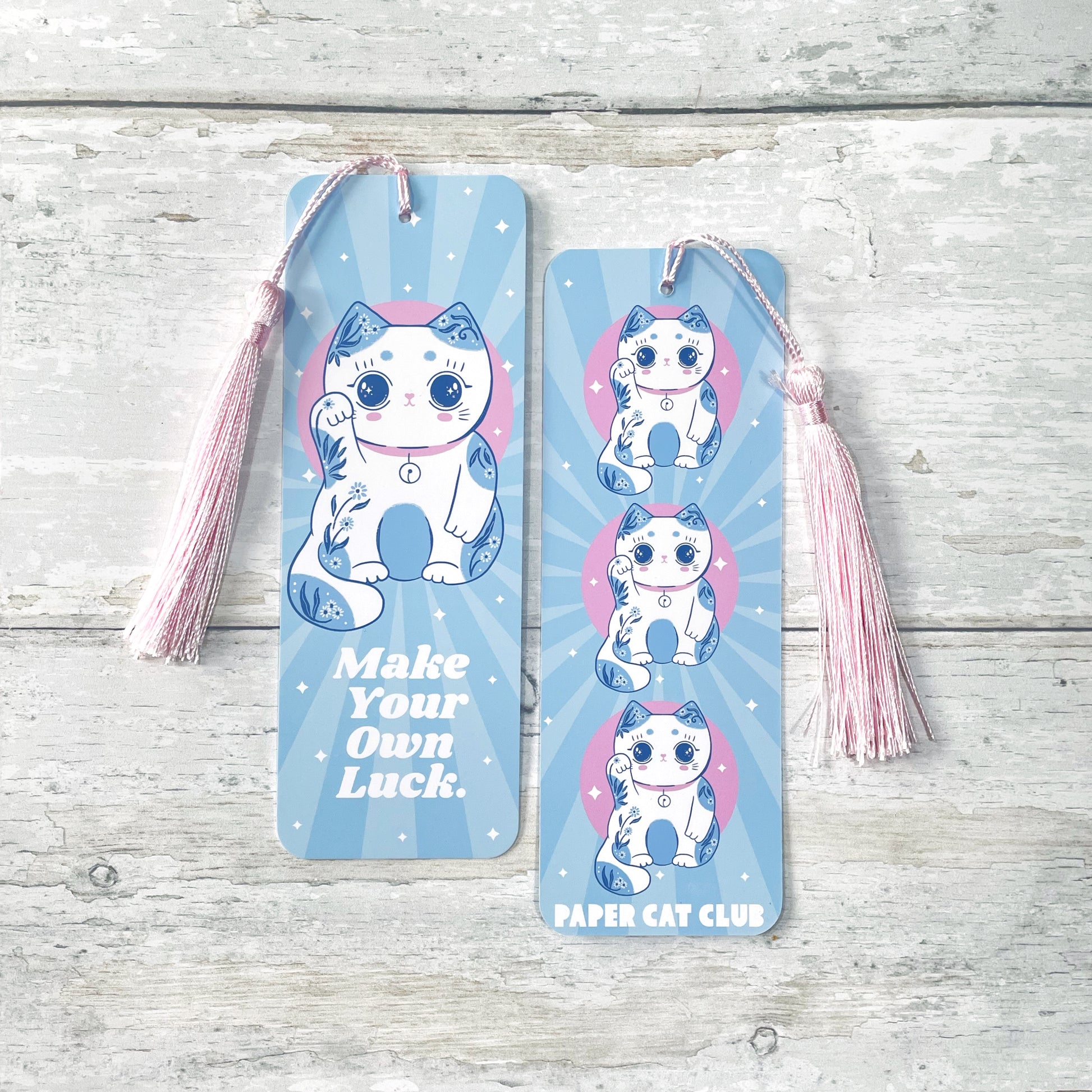 Front and back view of light blue lucky cat bookmark with pink tassel, featuring the phrase 'Make Your Own Luck,' perfect for kawaii style lovers and book lovers